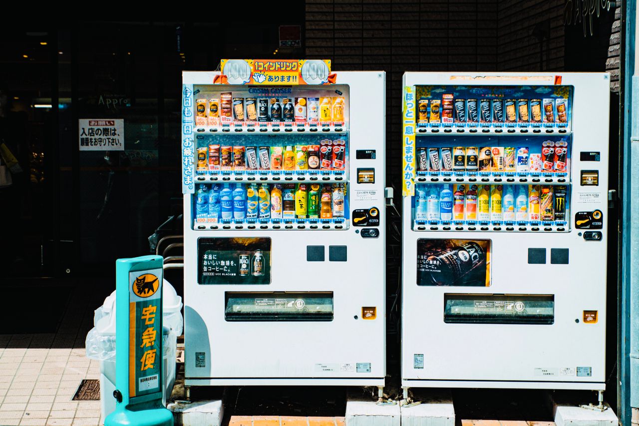 services-02 Colorful array of beverages in Japanese vending machines on a sunny city street.
